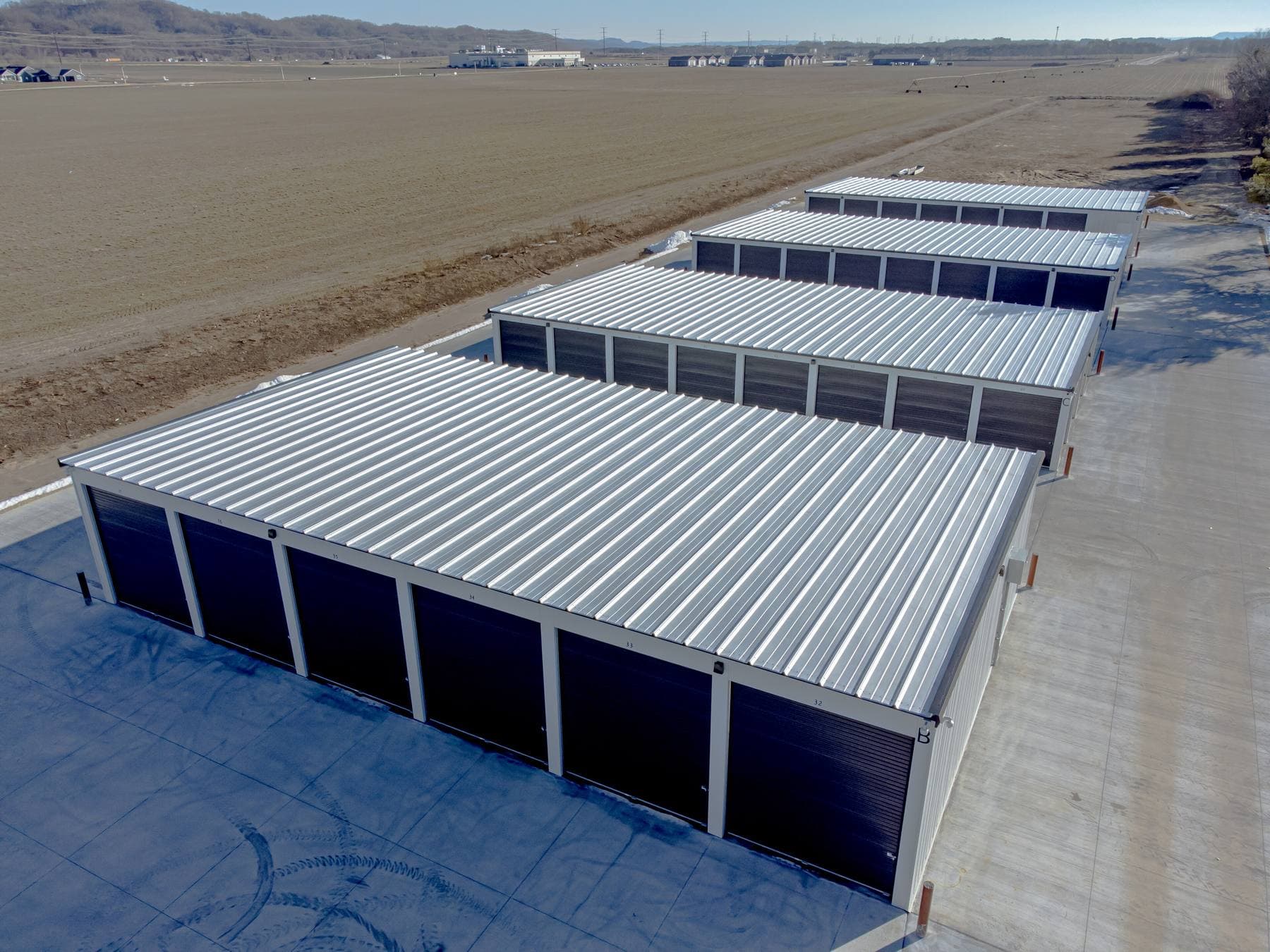 An aerial view of rows of new single-storey storage units with metal roofs and dark roll-up doors on open land