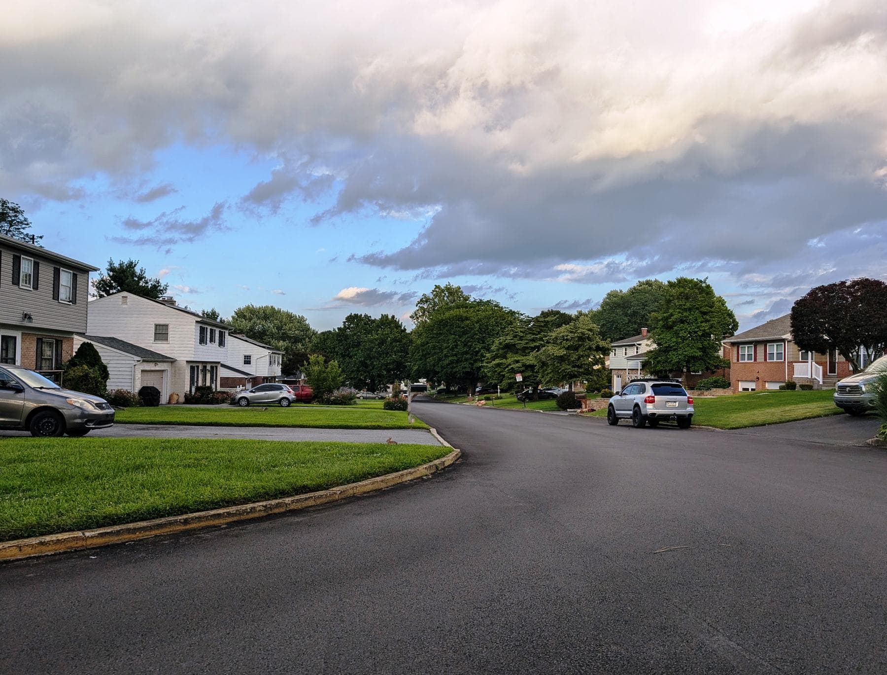 A quiet suburban street of houses with lawns and wide driveways under an evening sky
